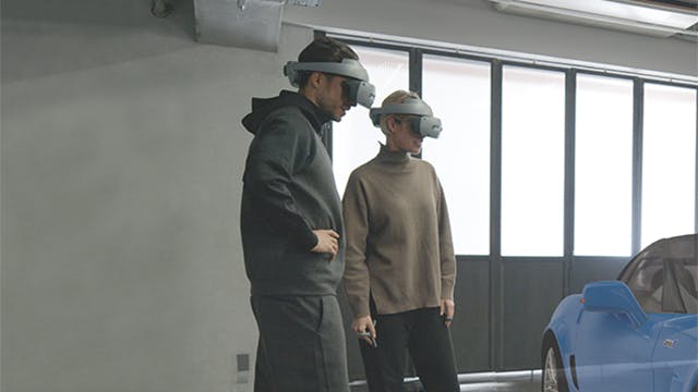 一男一女各自佩戴索尼 VR 头戴式设备，使用 Siemens NX Immersive Designer 软件制作蓝色跑车的虚拟模型。